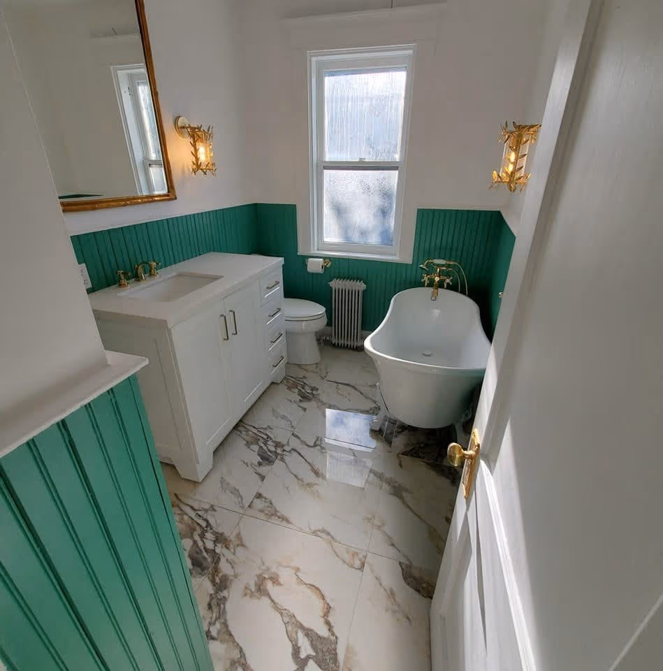 Finished bathroom with a freestanding clawfoot tub, green wall paneling, white vanity, and marble-look floor tile