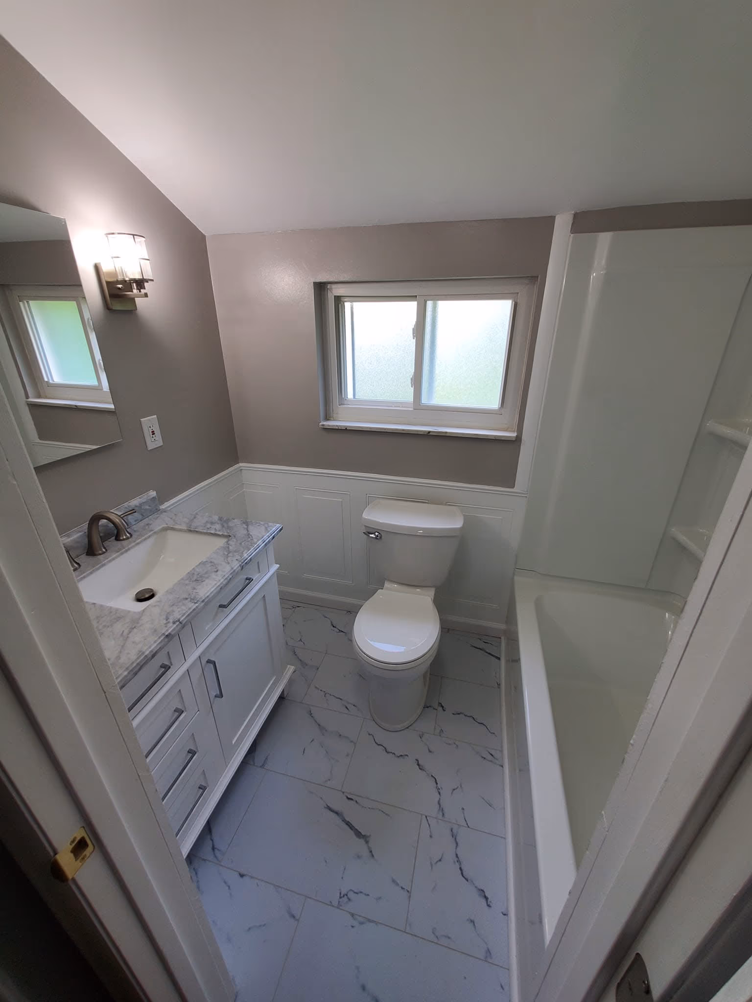 Finished gray bathroom with a white vanity, marble-look floor tile, bathtub, and storage cabinet