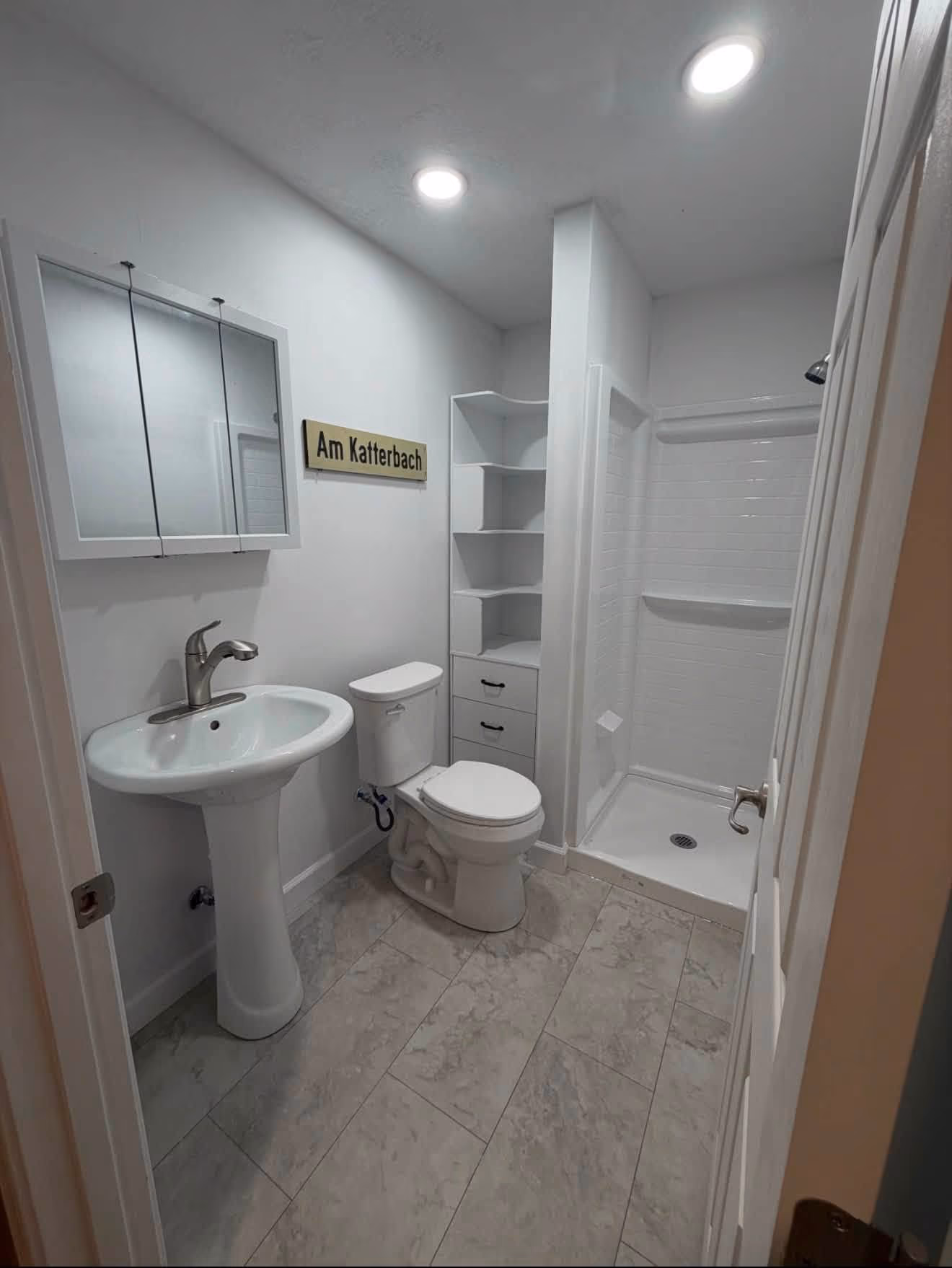 Finished compact bathroom with shower, pedestal sink, toilet, and built-in storage