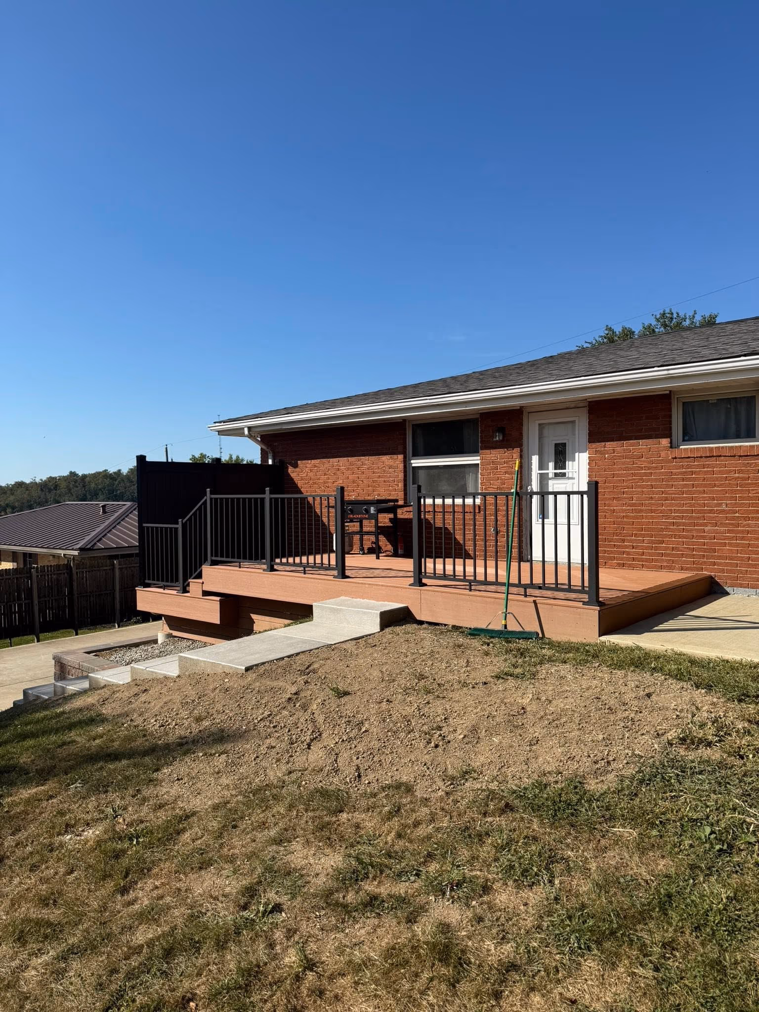 Brown deck with black railing behind a brick home